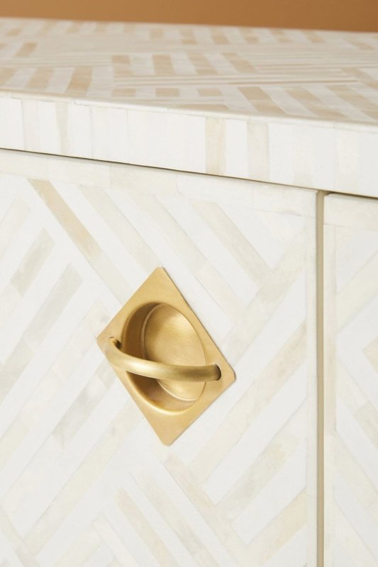 Close-up of a white optical bone inlay dresser drawer featuring a diamond-shaped solid brass recessed handle against a geometric chevron bone inlay surface pattern.