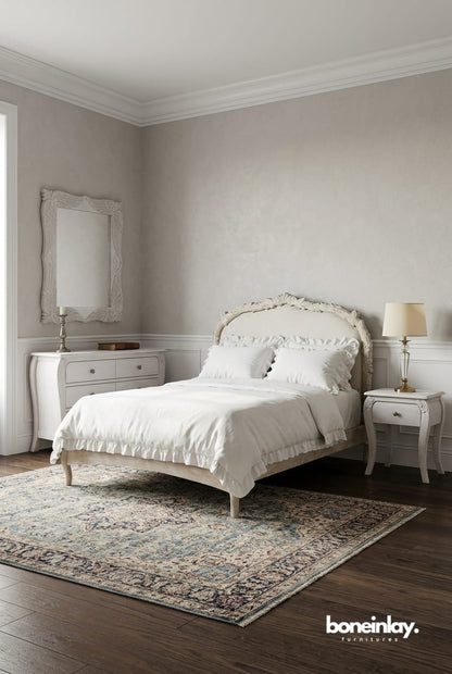 A curated lifestyle setting of the Menagerie bedroom suite, featuring a centerpiece hand-carved bed with an upholstered headboard in a neutral linen fabric. The set is flanked by matching cabriole-leg nightstands against a serene dusty blue wall, styled with a plush ivory rug and a minimalist floral chandelier to evoke a "Quiet Luxury" aesthetic.