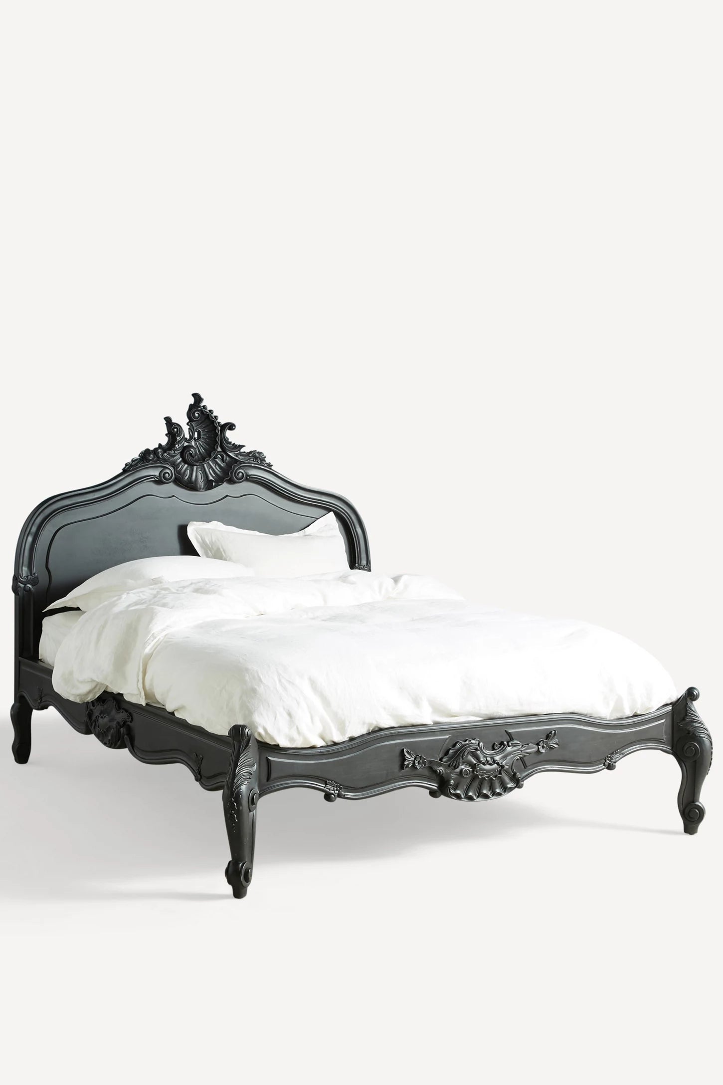 A perspective shot of the Menara bed highlighting the fluid, curved lines of the frame and the handcrafted floral carvings along the side rails and cabriole feet.