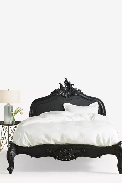 A direct front-facing view of the Menara black-carved bed frame with its striking, high-arched headboard featuring intricate Rococo-style scrollwork and a deep matte black finish.