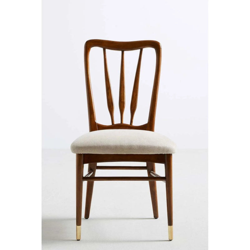 Front view of a mid-century modern solid wood dining chair with a curved spindle back, light beige upholstered seat, and brass-capped tapered legs.