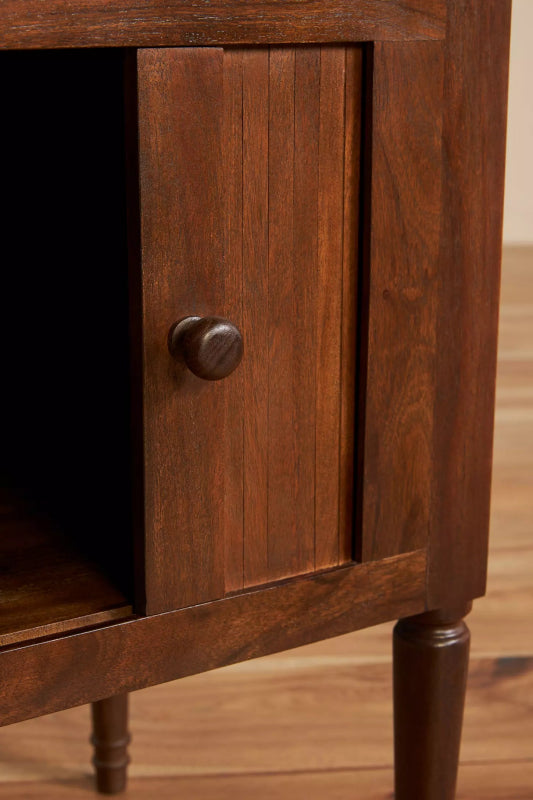 Close-up of a natural finish mid-century bedside table’s partially open cabinet door, showing vertical wood grain and a round knob.
