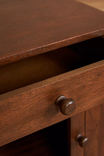 Close-up of a natural finish mid-century bedside table’s partially open drawer, round wooden knob, and tabletop edge.