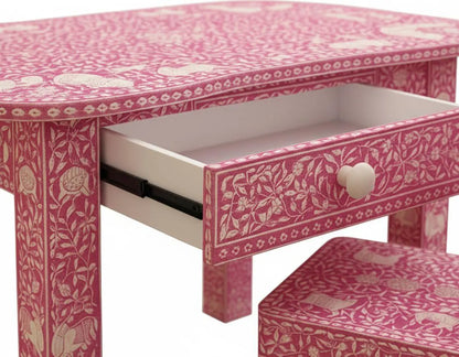 Close-up of a pink bone inlay kids desk with an open drawer, floral detailing, and a matching patterned chair seat.