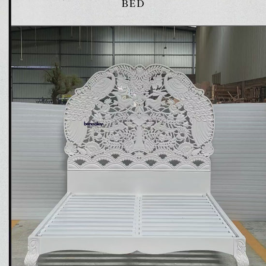 A grand, hand-carved solid wood bed frame finished in a pristine white satin. The monumental headboard features a high-relief "Peacock Woodland" scene, masterfully sculpted with intricate details of graceful peacocks, jumping rabbits, and songbirds amidst a lush canopy of blossoming trees and floral vines. The bed includes a robust slatted support system and elegant cabriole legs, each accented with delicate hand-carved leaf motifs. This artisanal piece highlights the depth and texture of traditional wood.