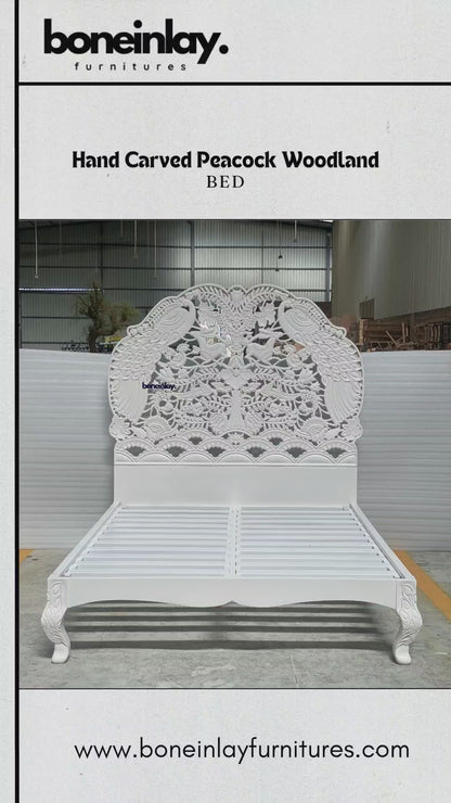 A grand, hand-carved solid wood bed frame finished in a pristine white satin. The monumental headboard features a high-relief "Peacock Woodland" scene, masterfully sculpted with intricate details of graceful peacocks, jumping rabbits, and songbirds amidst a lush canopy of blossoming trees and floral vines. The bed includes a robust slatted support system and elegant cabriole legs, each accented with delicate hand-carved leaf motifs. This artisanal piece highlights the depth and texture of traditional wood.