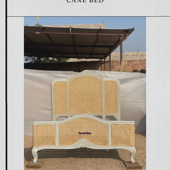 This video highlights a handcrafted French-design bed frame featuring light tan natural cane webbing inserts on both the three-panel headboard and the contoured footboard. The solid wood structure is finished in a vintage off-white hue, decorated with delicate floral crown carvings and supported by classic cabriole legs. Text overlays emphasize bespoke ordering benefits such as free worldwide delivery and customization options.