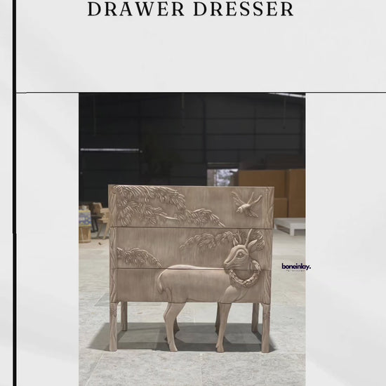 A three-drawer wooden dresser made from light-grained, uniquely hand-carved with a continuous wildlife and nature scene. The design features a prominent deer and a flying bird amidst lush trees and foliage, spanning across the drawer fronts for a seamless 3D effect. The land & sky dresser is finished with minimalist, integrated side handles and sturdy square legs, blending artisanal storytelling with functional furniture design.