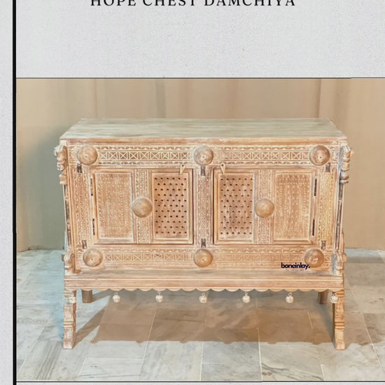 This video showcases a "Hand Carved Solid Wooden Sideboard Hope Chest Damchiya," a stunning piece of traditional Rajasthani furniture. The video highlights its intricate hand-carved geometric patterns, delicate perforated door panels, and distinctive hanging bell-style decorative accents along the base. The sideboard’s weathered finish and robust craftsmanship evoke a timeless, rustic charm, perfectly blending artisanal heritage with versatile home storage.