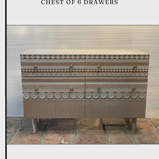 A wide, six-drawer wooden chest with intricate hand-carved geometric patterns on the drawer fronts. The light wood finish is accented by circular gold ring pulls and sits on four tapered white legs. The design features alternating rows of diamond, zigzag, and floral-inspired carvings