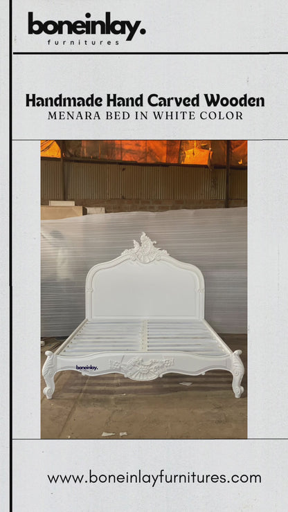 An advertisement video features a pristine white, handmade hand-carved wooden "Menara Bed" styled in elegant French Rococo design with an ornate shell-and-floral headboard, cabriole legs, and detailed relief carvings. The video pans smoothly across the empty platform frame inside a warehouse setting, showcasing its structural design and elaborate artisan craftsmanship up close. It concludes with a call-to-action screen displaying "Shop now," the website URL, and customer benefits like free worldwide deliver