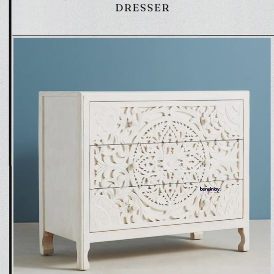 The dresser features a clean, white-washed finish with a large, intricate hand-carved mandala design extending across the front of all three drawers.
A hand is shown opening the middle drawer to reveal the natural grain of the solid wood interior and smooth sliding mechanism.