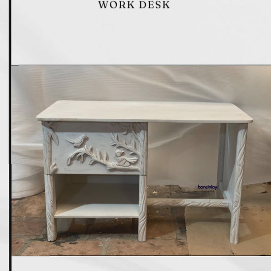 This video presents a detailed view of a handmade Ornithology Workdesk finished in a clean, vintage white. The camera highlights the intricate hand-carvings of birds resting on floral branches that decorate the single drawer front and side panels. It further showcases the desk's practical features, including a smooth tabletop, an open storage shelf, and twisted-effect carved legs