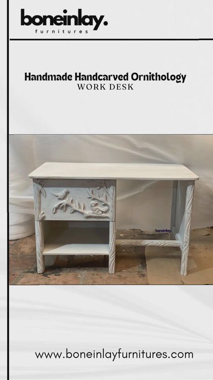 This video presents a detailed view of a handmade Ornithology Workdesk finished in a clean, vintage white. The camera highlights the intricate hand-carvings of birds resting on floral branches that decorate the single drawer front and side panels. It further showcases the desk's practical features, including a smooth tabletop, an open storage shelf, and twisted-effect carved legs
