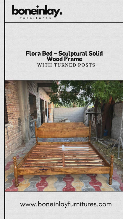 A promotional video showcases the Flora Bed, a wooden bed frame featuring a sleek, sculptural solid wood design with four elegant, turned posts at each corner. The video displays the empty wooden frame in an outdoor brick setting before transitioning to a fully furnished, styled bedroom, highlighting the bed's rustic yet refined aesthetic.