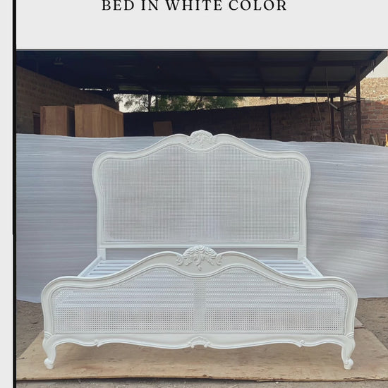 A factory video showcasing a handcrafted, solid wood French Provincial bed in a matte white finish. It features an arched headboard with natural caned panels and intricate, hand-carved floral motifs along the crest and cabriole legs. The video highlights the sturdy slatted support system and offers free worldwide delivery with customization options.