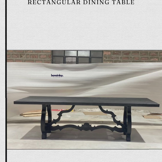 A factory video showcasing a solid wood Baroque trestle table with a hand-carved, sculptural base in matte black. The rectangular top features a textured finish, highlighting the artisanal quality of the handmade Indian design. The video promotes free worldwide delivery, customization, and bulk discounts.