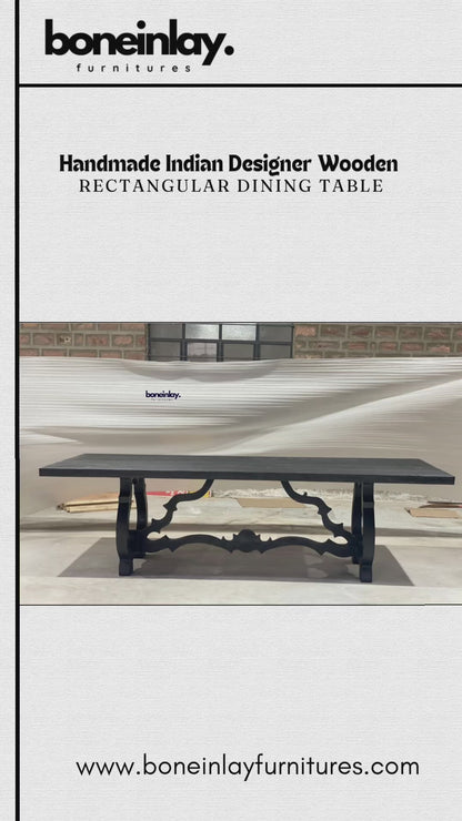 A factory video showcasing a solid wood Baroque trestle table with a hand-carved, sculptural base in matte black. The rectangular top features a textured finish, highlighting the artisanal quality of the handmade Indian design. The video promotes free worldwide delivery, customization, and bulk discounts.