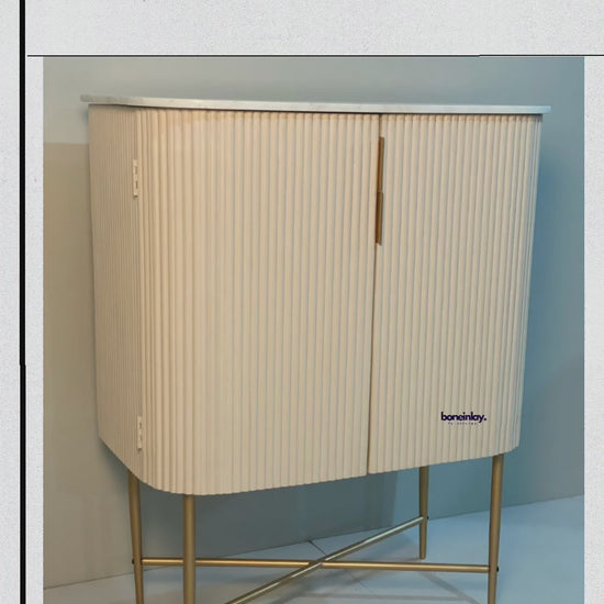 White fluted bar cabinet with rounded front corners and a brass X-leg base, shown in a branded product video.