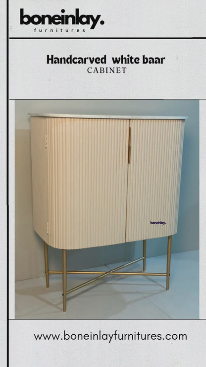 White fluted bar cabinet with rounded front corners and a brass X-leg base, shown in a branded product video.