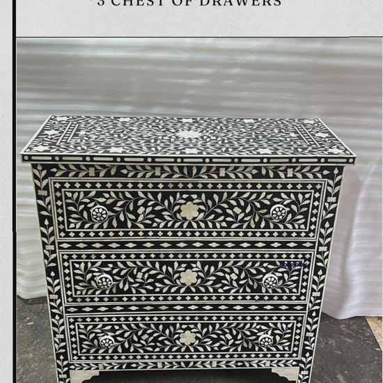 The "Bone Inlay Floral Design Black 3 Chest of Drawers" by boneinlay furnitures is an exquisite handcrafted piece. It features a striking black and white floral inlay pattern with three spacious drawers, each adorned with a simple white knob. The chest is finished with a classic base and is showcased in a video that highlights its intricate details and craftsmanship.