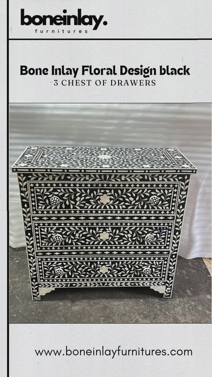 The "Bone Inlay Floral Design Black 3 Chest of Drawers" by boneinlay furnitures is an exquisite handcrafted piece. It features a striking black and white floral inlay pattern with three spacious drawers, each adorned with a simple white knob. The chest is finished with a classic base and is showcased in a video that highlights its intricate details and craftsmanship.