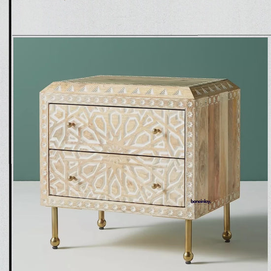 Handcrafted wooden nightstand with white bone inlay featuring a central starburst mandala and geometric borders. Includes two drawers with brass knobs and slender gold-finished legs. Video demonstrates smooth drawer opening and detailed artisanal construction