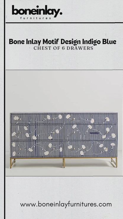 A close-up video showcasing a large, six-drawer indigo blue chest of drawers featuring a striking white bone inlay pattern. The design consists of thin horizontal stripes across the entire piece, accented by delicate floral motifs and round brass knobs. A person is shown opening the drawers, revealing a spacious, dark navy blue interior, emphasizing both the chest’s functionality and its artisanal, textured finish.