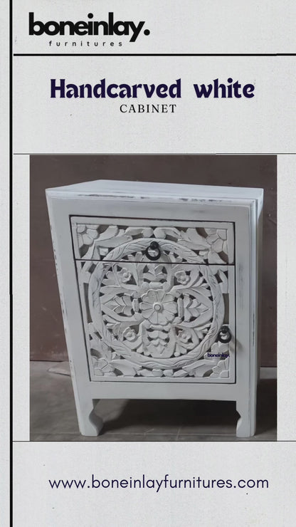 Hand-carved solid wood bedside table with a rustic finish, featuring a circular floral motif across the drawer and cabinet door, dark ring pulls, and shaped legs.