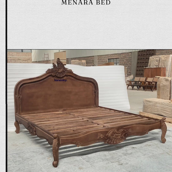 An advertisement video features a rich brown, hand-carved solid wooden "Menara Bed" styled in elegant French Rococo design with an intricate shell-and-floral crest headboard, cabriole legs, and ornate relief carvings. The camera pans across the platform frame inside a spacious warehouse, highlighting the warm wood grain and artisan details from multiple sweeping angles. It concludes with a call-to-action screen displaying "Shop now," the website URL, and consumer incentives including free worldwide delivery