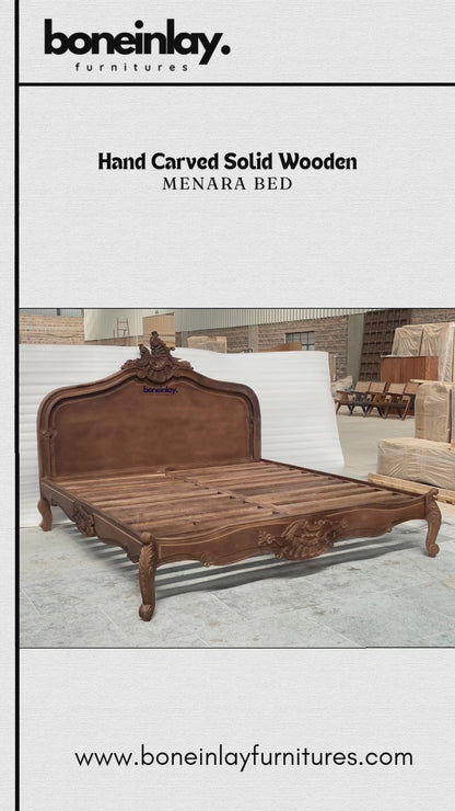 An advertisement video features a rich brown, hand-carved solid wooden "Menara Bed" styled in elegant French Rococo design with an intricate shell-and-floral crest headboard, cabriole legs, and ornate relief carvings. The camera pans across the platform frame inside a spacious warehouse, highlighting the warm wood grain and artisan details from multiple sweeping angles. It concludes with a call-to-action screen displaying "Shop now," the website URL, and consumer incentives including free worldwide delivery