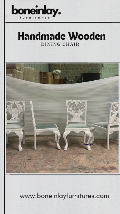 The video showcases intricately hand-carved wooden dining chairs, each featuring a unique animal or nature-inspired motif on the backrest, including an owl, a deer, a tree, and a rabbit. The chairs are painted in a distressed white finish with soft sage green cushioned seats, blending rustic charm with artistic craftsmanship. The scenes highlight the fine detailing of the carvings and the overall elegant design suitable for a menagerie-themed dining space.