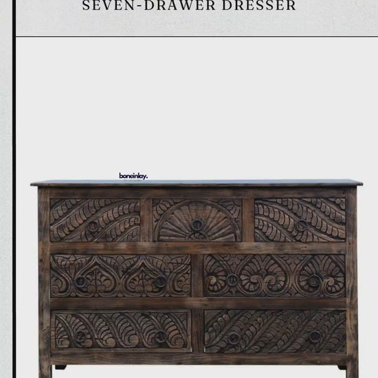 The dresser features a rich, dark wood finish with intricate hand-carved floral and fan-like motifs across all seven drawers.
A hand is shown opening one of the top drawers to demonstrate the smooth functionality and solid wood interior. 