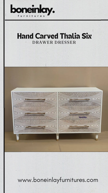 A modern six-drawer white dresser with intricate hand-carved geometric sunburst patterns on each drawer front. The piece features long gold horizontal handles and stands on four white tapered legs with gold metal tips. The high-relief carving creates a textured, two-tone effect between the white surface and natural wood grooves.