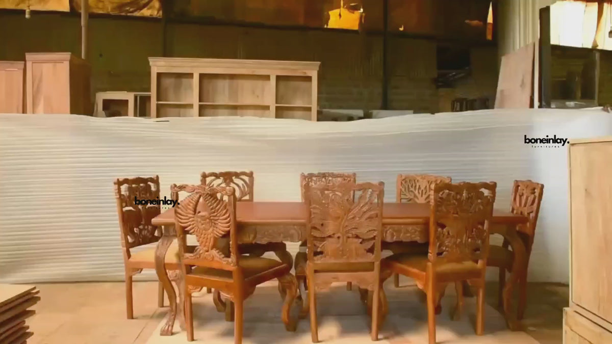 This video showcases an artisan-crafted solid wood dining set with a rich honey-brown finish, featuring an expansive rectangular table and chairs with intricate hand-carved backrests. Each chair displays a unique wildlife or nature motif, including a majestic owl with outspread wings, a peacock, an elephant, and a tree of life, all exhibiting remarkable 3D detail. The set is filmed in an artisanal workshop, emphasizing the traditional wood-carving heritage and the high-quality craftsmanship that makes this 