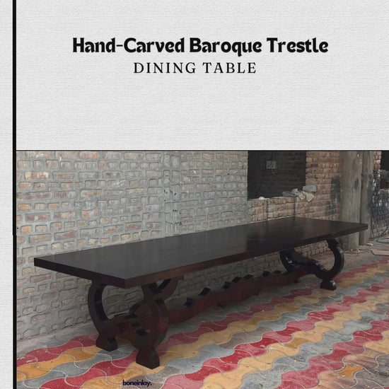 A promotional video showcases a Hand-Carved Baroque Trestle Dining Table, featuring a dark-stained wood finish and an intricately designed base. The clip frames the elongated table from multiple angles in an outdoor space before transitioning to a staged dining room setting, where it is surrounded by elegant chairs under a chandelier.