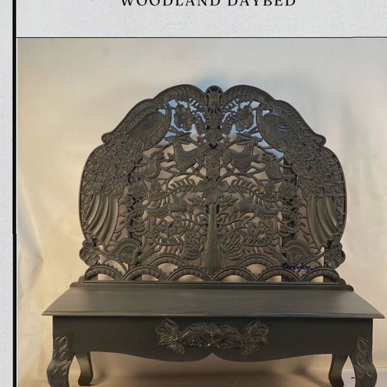 This video showcases a "Handcarved Custom Black Peacock Woodland Daybed," an exquisite piece of furniture featuring a tall, arched backrest with detailed openwork carvings of peacocks, floral patterns, and nature motifs. The entire piece is finished in a bold matte black, creating a dramatic and sophisticated aesthetic. The camera highlights the artistry of the hand-carved details, from the crown of the backrest down to the floral-carved apron and curved legs, blending traditional craftsmanship with a moder