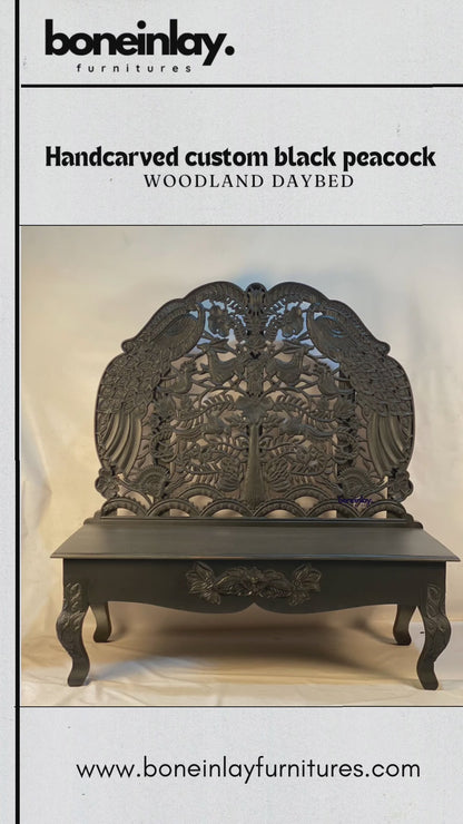 This video showcases a "Handcarved Custom Black Peacock Woodland Daybed," an exquisite piece of furniture featuring a tall, arched backrest with detailed openwork carvings of peacocks, floral patterns, and nature motifs. The entire piece is finished in a bold matte black, creating a dramatic and sophisticated aesthetic. The camera highlights the artistry of the hand-carved details, from the crown of the backrest down to the floral-carved apron and curved legs, blending traditional craftsmanship with a moder