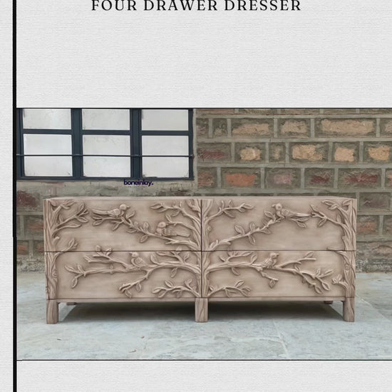 A wide, four-drawer hand-carved wooden dresser with a light natural finish. The entire front is decorated with a deeply textured 3D carving of birds on leafy tree branches. The piece has a contemporary yet rustic aesthetic with clean lines and short, square legs