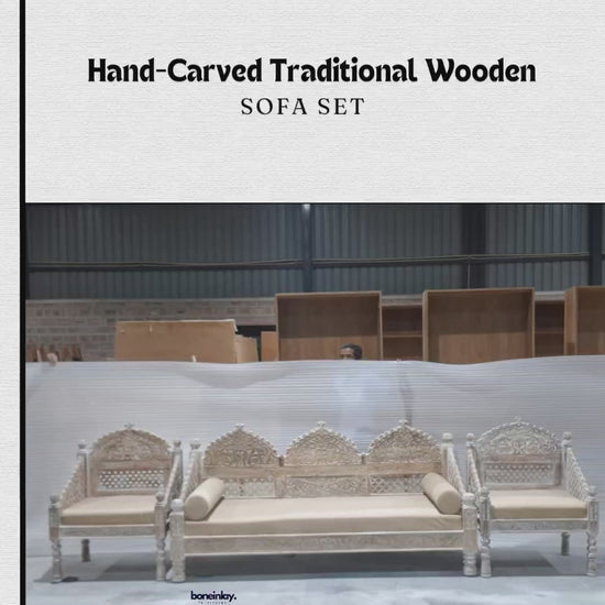 A showcase of the Hand-Carved Maharaja Triple Arch Sofa Set in a stunning distressed white-wash finish. This artisanal collection features a grand three-seater sofa and two matching armchairs, all meticulously hand-carved from premium solid wood. The design is defined by its majestic triple-arched backrests, intricate floral lattice (jali) work, and high-relief botanical carvings. Each piece includes plush, neutral-toned seat cushions and stands on masterfully turned legs with sculptural accents. The video 