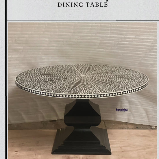 A round, handmade bone inlay dining table featuring an intricate black and white floral and leafy pattern that radiates outwards from the center. The ornate, circular tabletop sits atop a sturdy, geometric pedestal base finished in solid matte black. The rim of the tabletop is detailed with a contrasting black and white checkerboard border.