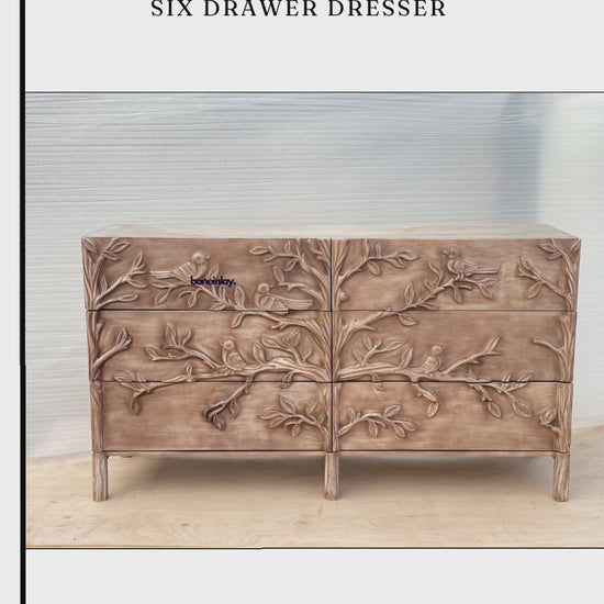 A large, six-drawer hand-carved wooden dresser featuring a detailed ornithology design of birds and tree branches across the entire front. The piece has a light, whitewashed natural finish and stands on four short, square legs, showcasing a blend of rustic charm and intricate craftsmanship.
