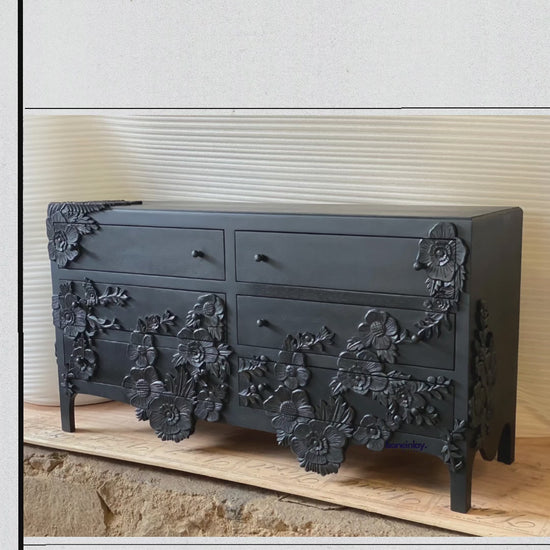 striking dresser is finished in a bold, matte black and is characterized by its high-relief, hand-carved floral appliqués. The 3D floral designs wrap around the corners and sprawl across the drawer fronts, creating a dramatic, textured silhouette.