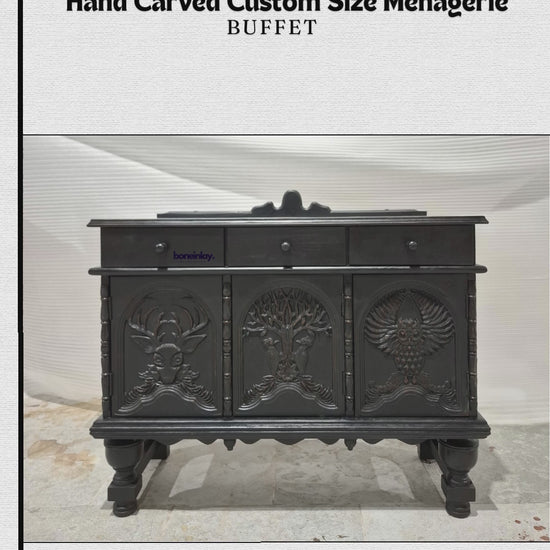 A matte-black hand-carved buffet features three top drawers and three lower cabinet doors detailed with intricate wildlife and nature reliefs, including a stag head and a tree. The video showcases its smooth drawers, interior storage shelves, and sturdy carved legs, highlighting the artisan craftsmanship. 