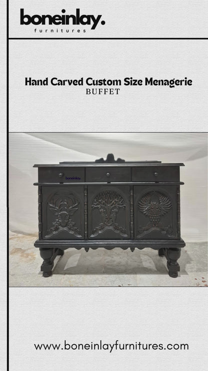A matte-black hand-carved buffet features three top drawers and three lower cabinet doors detailed with intricate wildlife and nature reliefs, including a stag head and a tree. The video showcases its smooth drawers, interior storage shelves, and sturdy carved legs, highlighting the artisan craftsmanship. 