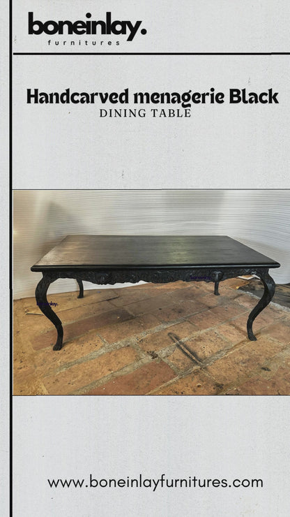A large rectangular black dining table with a detailed hand-carved apron featuring a lion's head and forest animals. The table has four curved cabriole legs with ornate leaf carvings and ball-and-claw feet, all in a matte black finish.