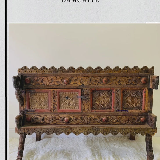 This video showcases a meticulously handcrafted antique Indian Damchiye, a traditional dowry chest featuring ornate wood carvings and vibrant, hand-painted accents. The camera pans across the detailed floral and geometric relief work, highlighting the hinged door storage and the piece's rustic, heritage-inspired aesthetic. This unique, masterfully crafted chest blends historical cultural artistry with functional, decorative storage for an upscale interior.