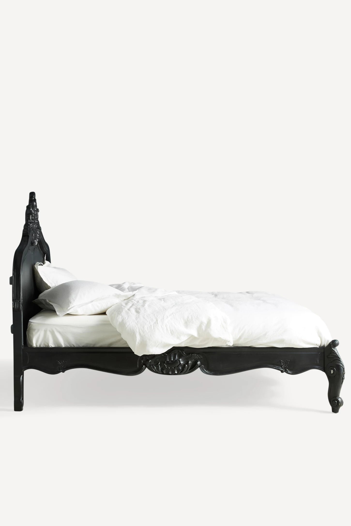 A sleek side view of the Menara bed frame without bedding, showcasing the solid construction and the elegant silhouette of the arched headboard and footboard.