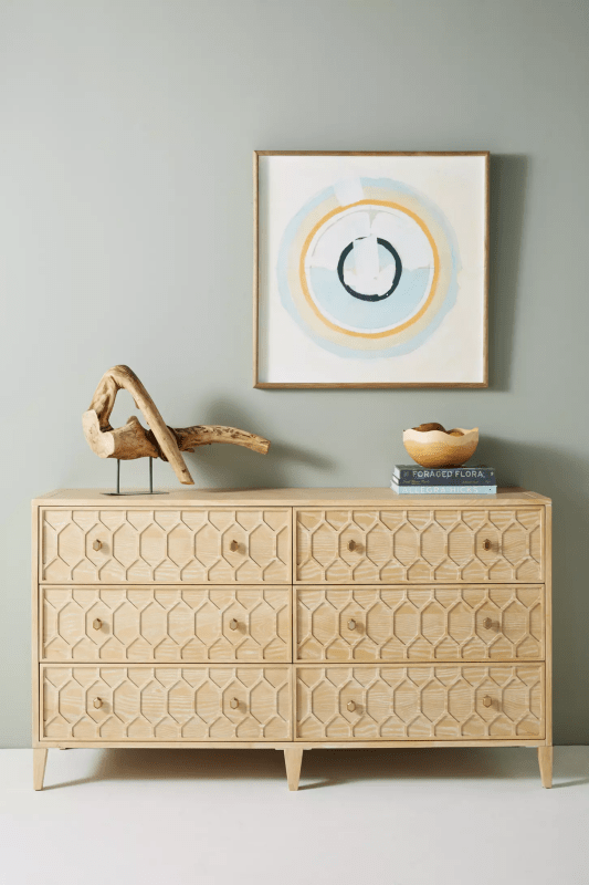 A 6-drawer solid wood dresser with a hand-carved textured trellis pattern in a light natural finish, styled with organic decor and minimalist art.