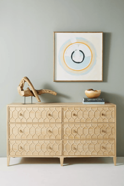 A 6-drawer solid wood dresser with a hand-carved textured trellis pattern in a light natural finish, styled with organic decor and minimalist art.